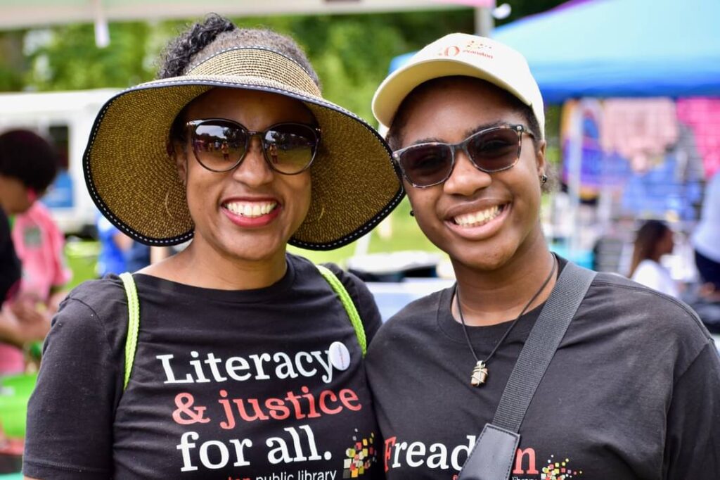 Two people smiling, one wearing a t-shirt that says "Literacy and Justice for all."